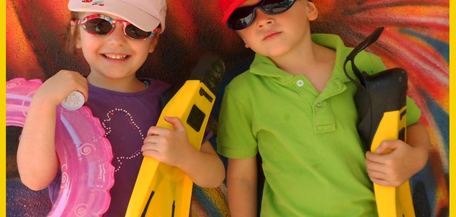 Kinderferienpass Gelber Rahmen. Zwei Kinder mit Sonnenbrillen, Schwimmreifen und Taucherflossen.