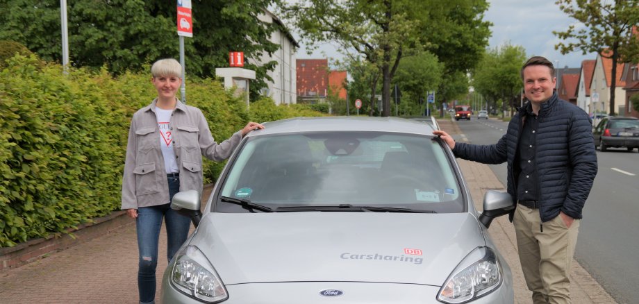 Neustadts Bürgermeister Dominic Herbst (links) und die Klimaschutzmanagerin Wendy Pfeil (links) werben für die Gutscheinaktion von Flinkster. Die beiden Personen stehen links und rechts neben einem Flinksterwagen an der Nineburgser Str. 31.